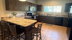 A kitchen with a granite countertop, dark cabinets, a central island with chairs, and a pendant light. - Brigham's Mill Retreat Between Grand Teton & Yellowstone National Parks (Rexburg)