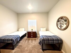 A bedroom with two single beds, a dresser, a window with blinds, and a wall decoration. - Brigham's Mill Retreat Between Grand Teton & Yellowstone National Parks (Rexburg)