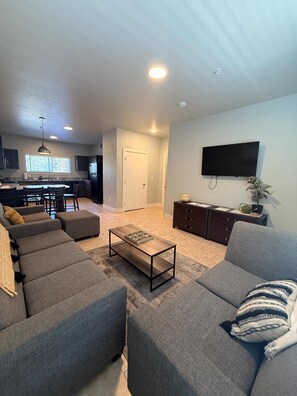 A modern living room with grey sofas, a coffee table, and a flat-screen TV mounted on the wall. - Brigham's Mill Retreat Between Grand Teton & Yellowstone National Parks (Rexburg)