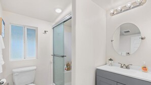 Une salle de bain comprenant des toilettes, une douche à parois de verre, un meuble-lavabo avec un miroir et un évier.