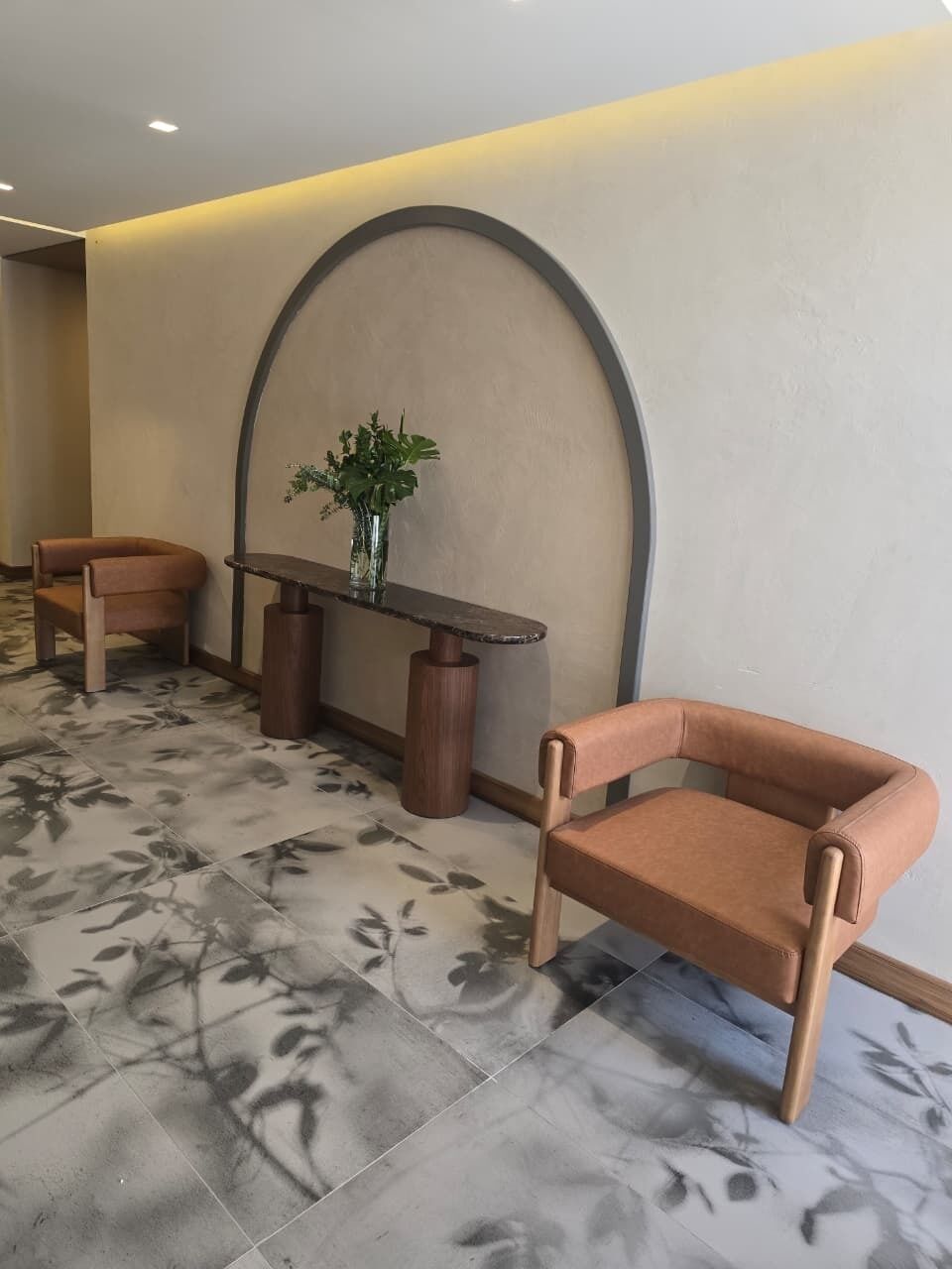 Una habitación con una pared curva, una mesa redonda, dos sillas y un florero con plantas.