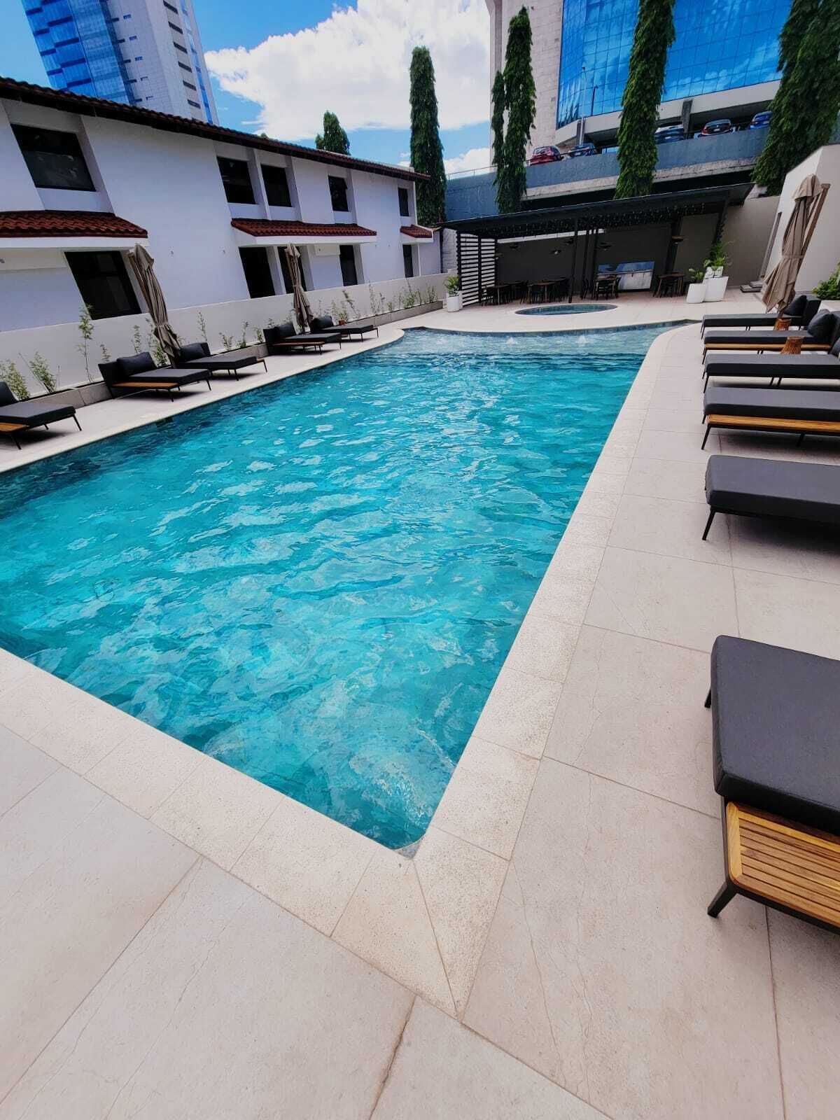A rectangular swimming pool with lounge chairs on one side and a building in the background.