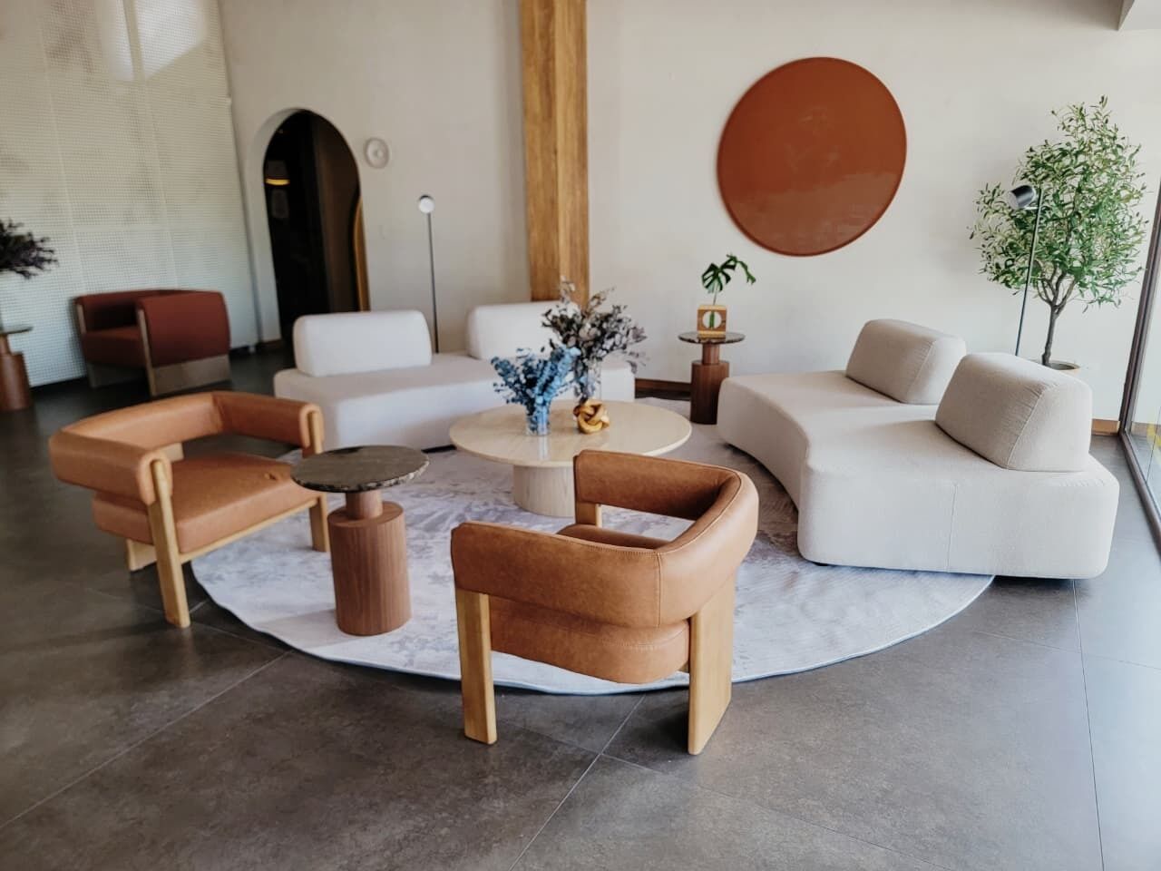 Una sala moderna con una mesa redonda, sillones de cuero, un sofá y un espejo grande y redondo en la pared.