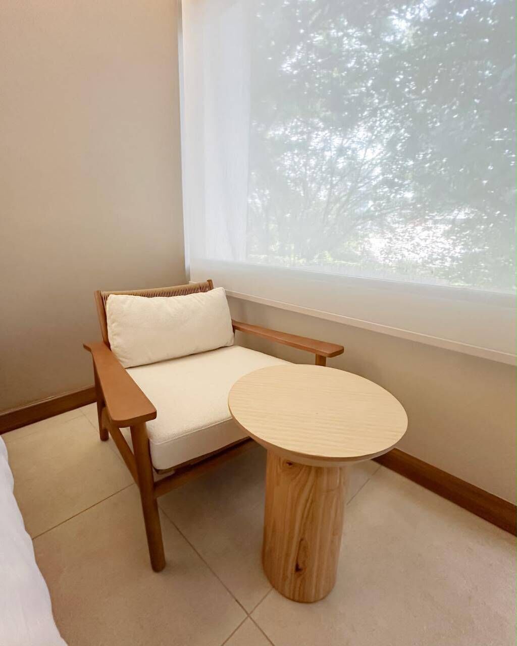 Une pièce d’angle avec une chaise en bois, une table ronde et une fenêtre donnant sur des arbres.