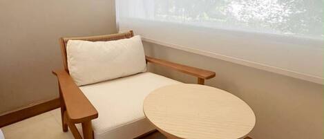 Une pièce d’angle avec une chaise en bois, une table ronde et une fenêtre donnant sur des arbres.