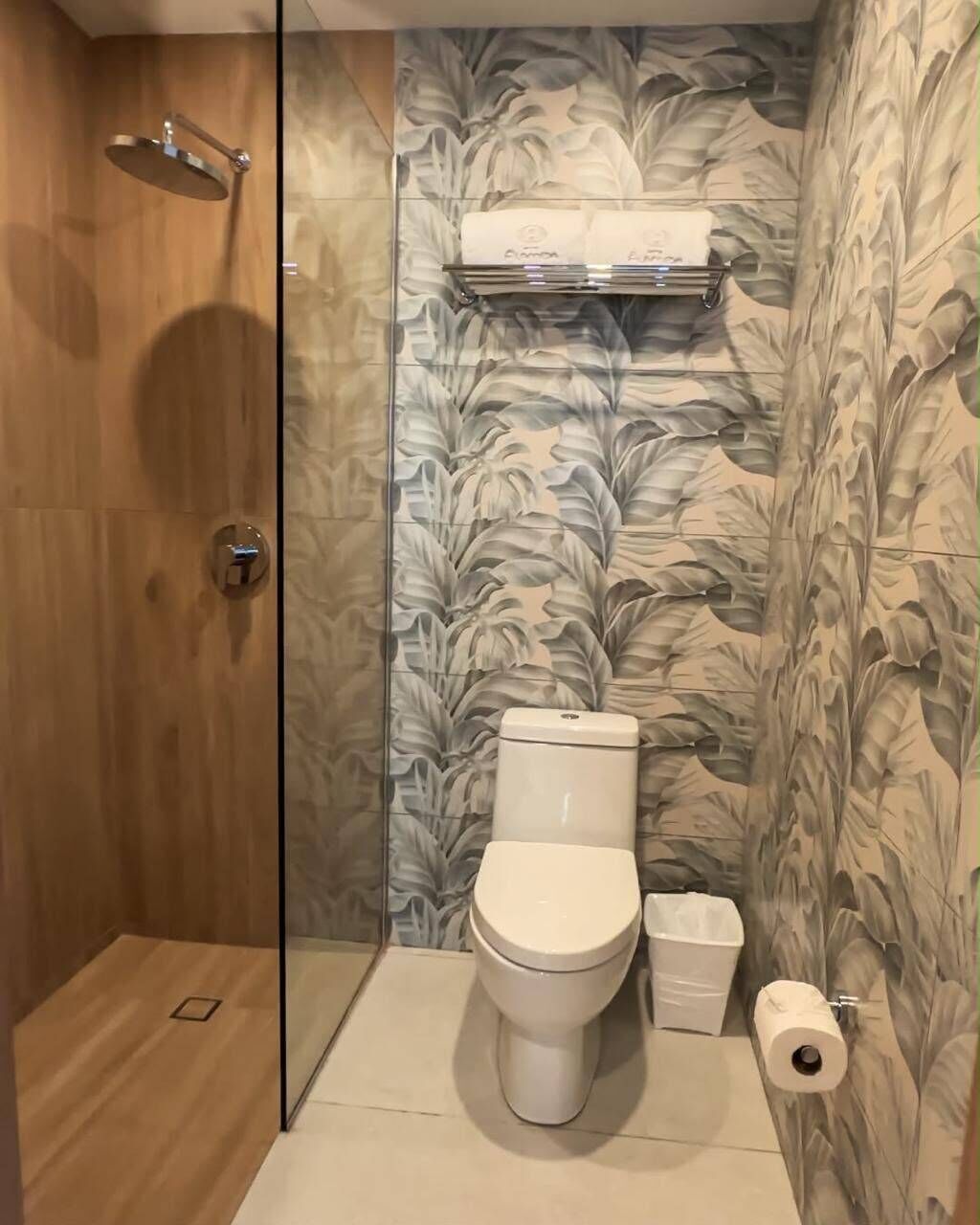 A bathroom with a toilet, a shower, a towel rack, and a trash bin.
