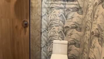 A bathroom with a toilet, a shower, a towel rack, and a trash bin.