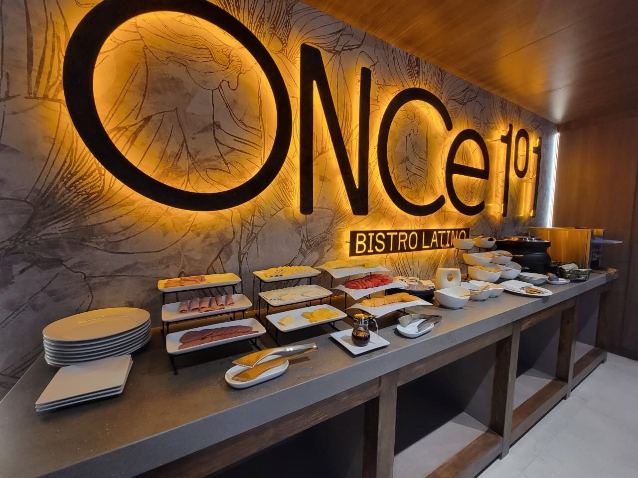 Montaje de bufé con un cartel que dice 'ONCE 101 BISTRO LATINO' y diferentes alimentos presentados en bandejas.