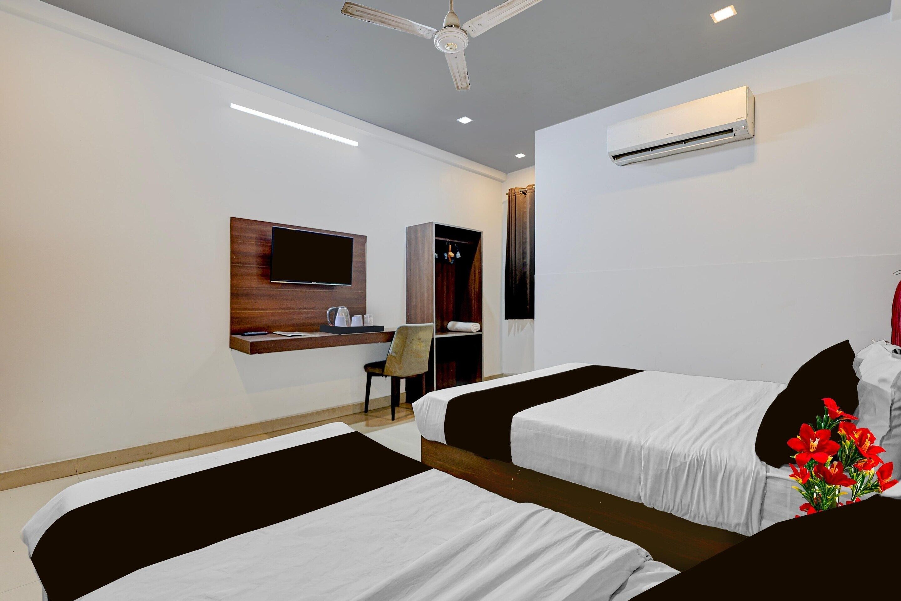 A hotel room with two beds, a TV, a desk, and an air conditioning unit.