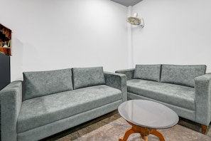 Ein modernes Wohnzimmer mit zwei grauen Sofas, einem kleinen runden Couchtisch und einem Wandventilator.