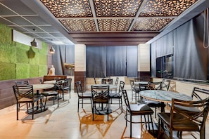 A restaurant interior with a modern design, featuring a patterned ceiling, green wall accents, and a mix of round and square tables with chairs.