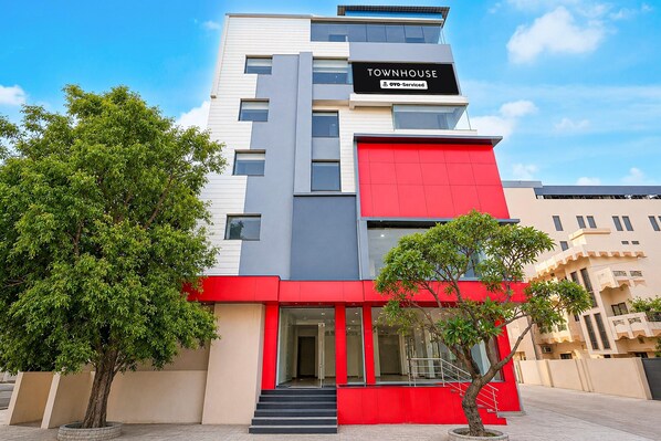Un immeuble à plusieurs étages, doté d’une façade rouge et grise bien visible, d’une enseigne indiquant qu’il est exploité par OYO, et d’un escalier menant à l’entrée.