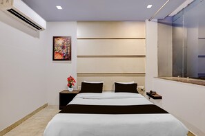 Ein Hotelzimmer mit einem Bett, einem Nachttisch, einer Vase mit Blumen, einem Gemälde an der Wand und einem Fenster.