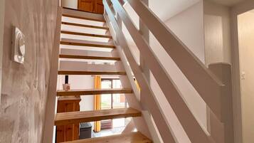 A wooden staircase with white railings leading to a room with a wooden ceiling and a window.