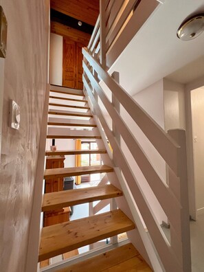 Eine Holztreppe mit weißen Geländern führt zu einem Raum mit Holzboden und einem Fenster.