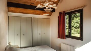 A bedroom with a bed, a wardrobe, a window with curtains, and a ceiling light fixture.