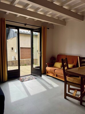 Eine offene Schiebetür führt zu einem Balkon, wo ein Holztisch und eine Couch mit Kissen stehen.