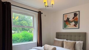 Una camera da letto con un letto, una finestra con tende, un quadro appeso al muro e un lampadario.