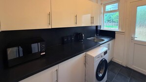 Una cucina moderna con mobili bianchi, un piano di lavoro nero, una lavatrice integrata e una finestra che fa entrare luce naturale.