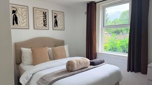 Una camera da letto con un letto, una finestra con tende e tre quadri appesi al muro.