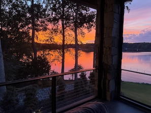 Ein Zimmer mit Blick auf einen Sonnenuntergang über einem Gewässer, Steinmauern und einem Balkongeländer.