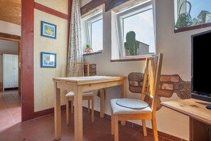 Een kamer met een houten bureau, een stoel, een televisie en een raam met uitzicht op een huis.
