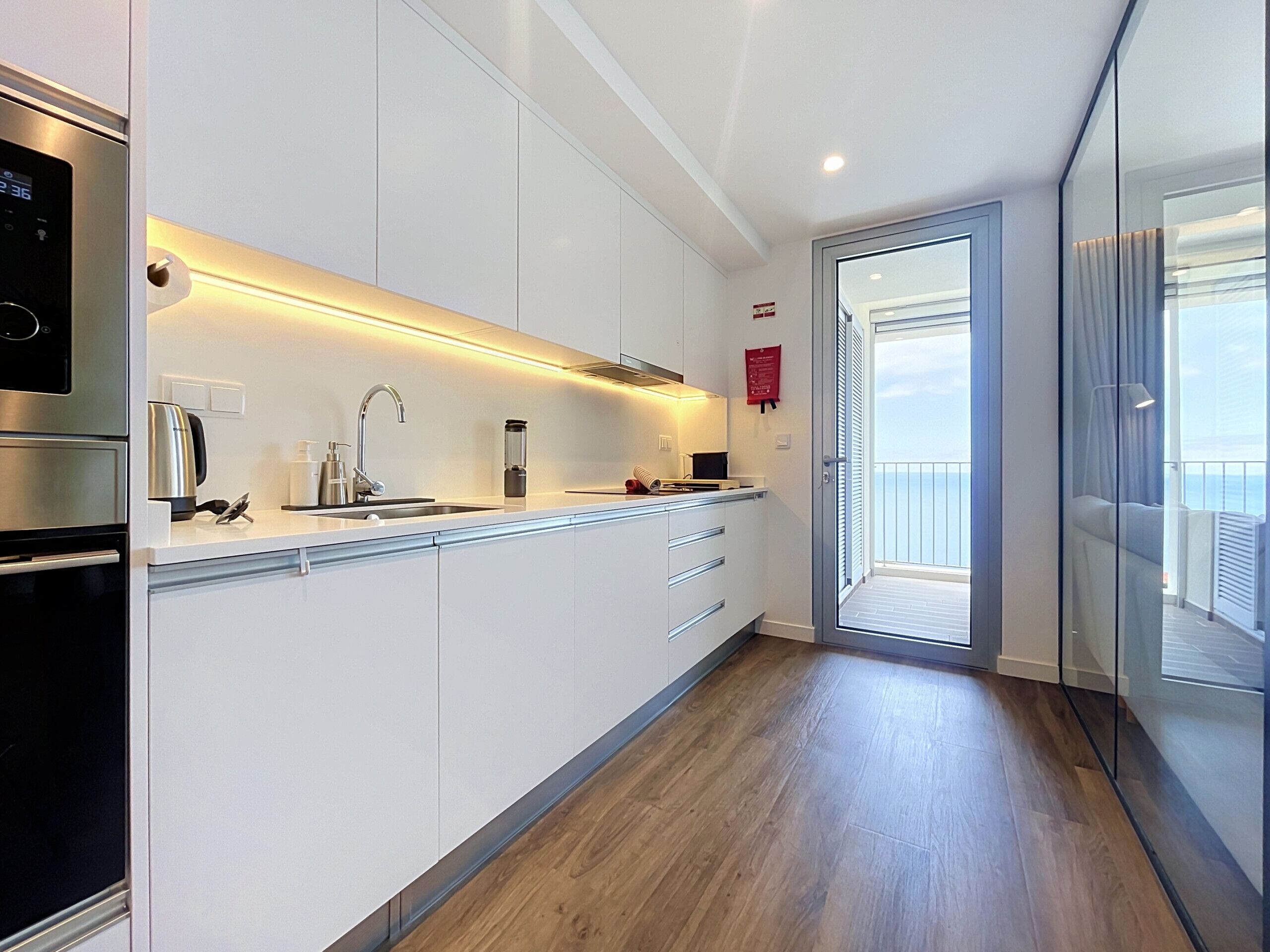 A modern kitchen with a built-in oven, stainless steel appliances, and a wooden floor.