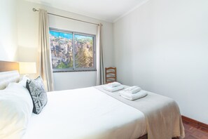 A hotel room with a bed, a window with curtains, a wooden chair, and a view of a rocky landscape. - Bella s Place Apartment by Atlantic Holiday (Santa Cruz)
