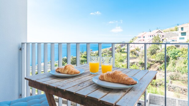 A wooden table with croissants and orange juice on a balcony overlooking a coastal view. - Bella s Place Apartment by Atlantic Holiday (Santa Cruz)