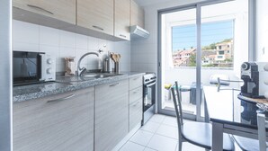 A modern kitchen with a microwave, toaster, and stove, a sink, and a view of a balcony with buildings. - Bella s Place Apartment by Atlantic Holiday (Santa Cruz)