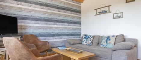 A living room with a striped wall, a sofa, two armchairs, a coffee table, and a television.