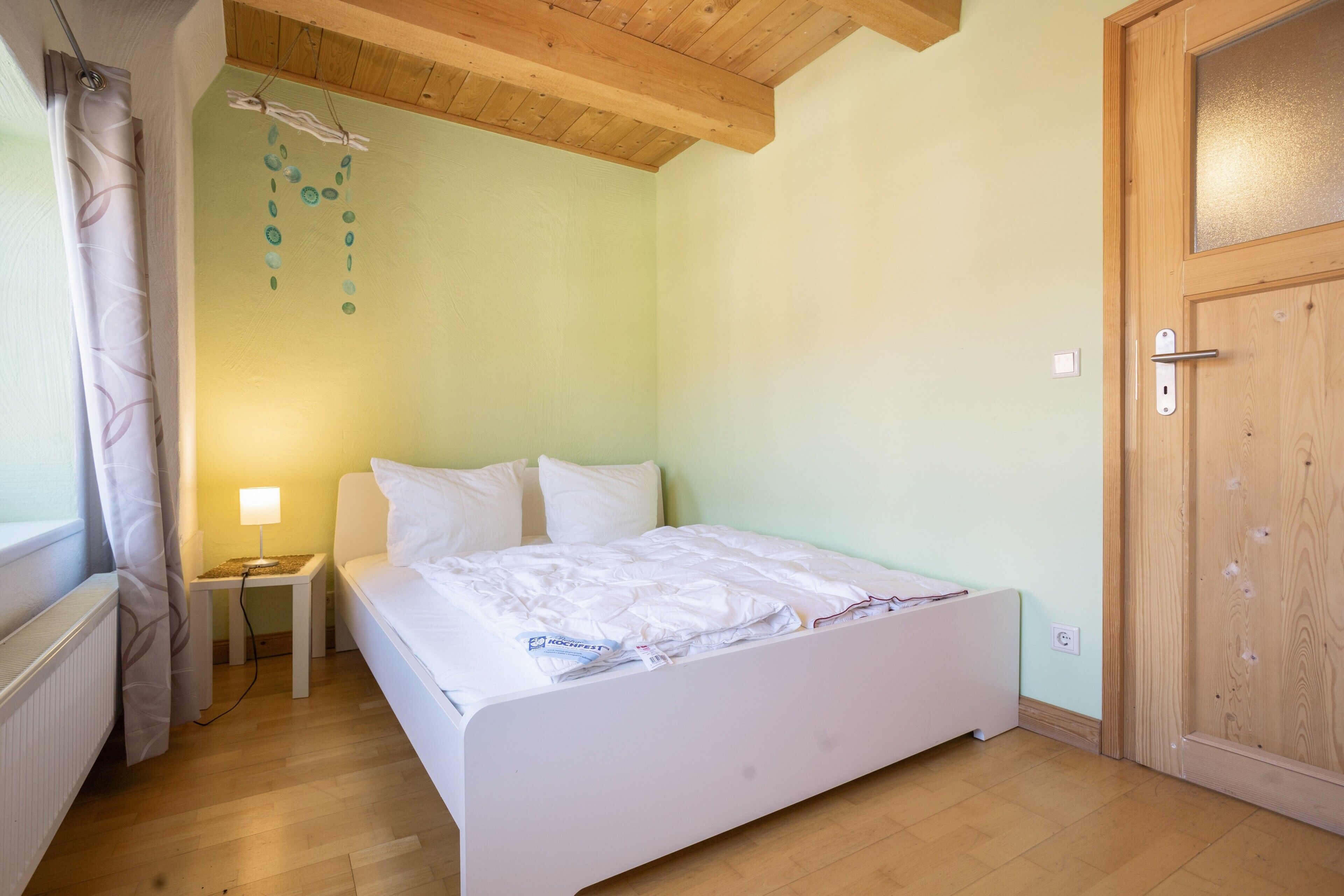 A bedroom with a bed, bedside table, lamp, and a wooden door.