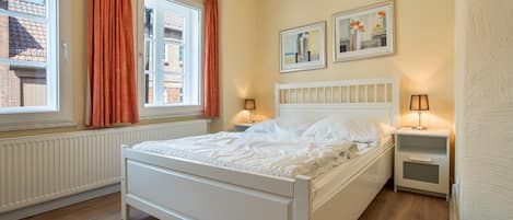 A bedroom with a bed, two bedside tables, a window with curtains, and two wall-mounted pictures.