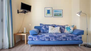 Ein Zimmer mit einem blauen Sofa, einem kleinen Beistelltisch, einer Stehlampe und zwei gerahmten Bildern an der Wand.