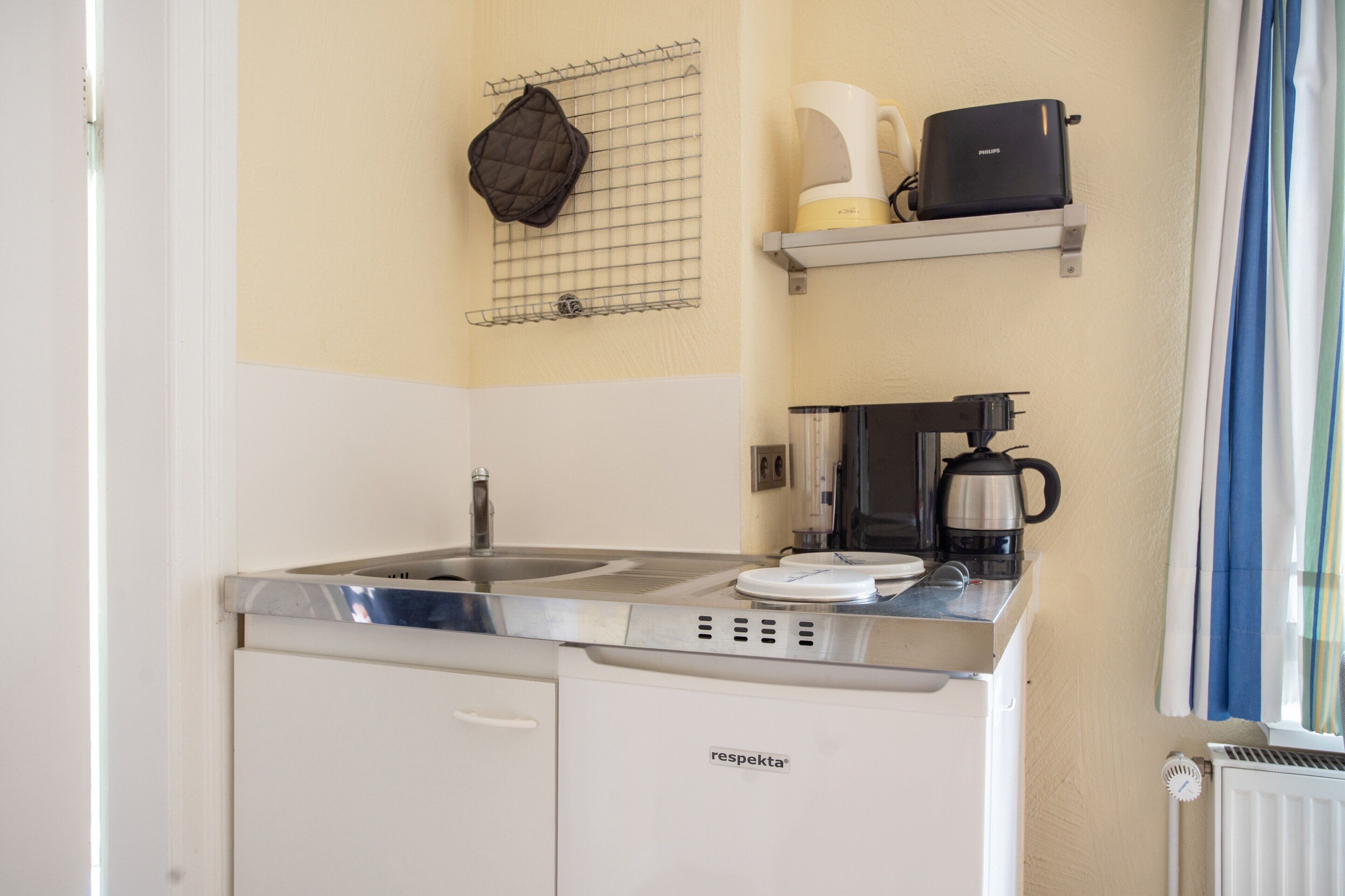 Une petite cuisine équipée d’une cuisinière intégrée, d’une machine à café et d’une bouilloire posées sur le plan de travail.
