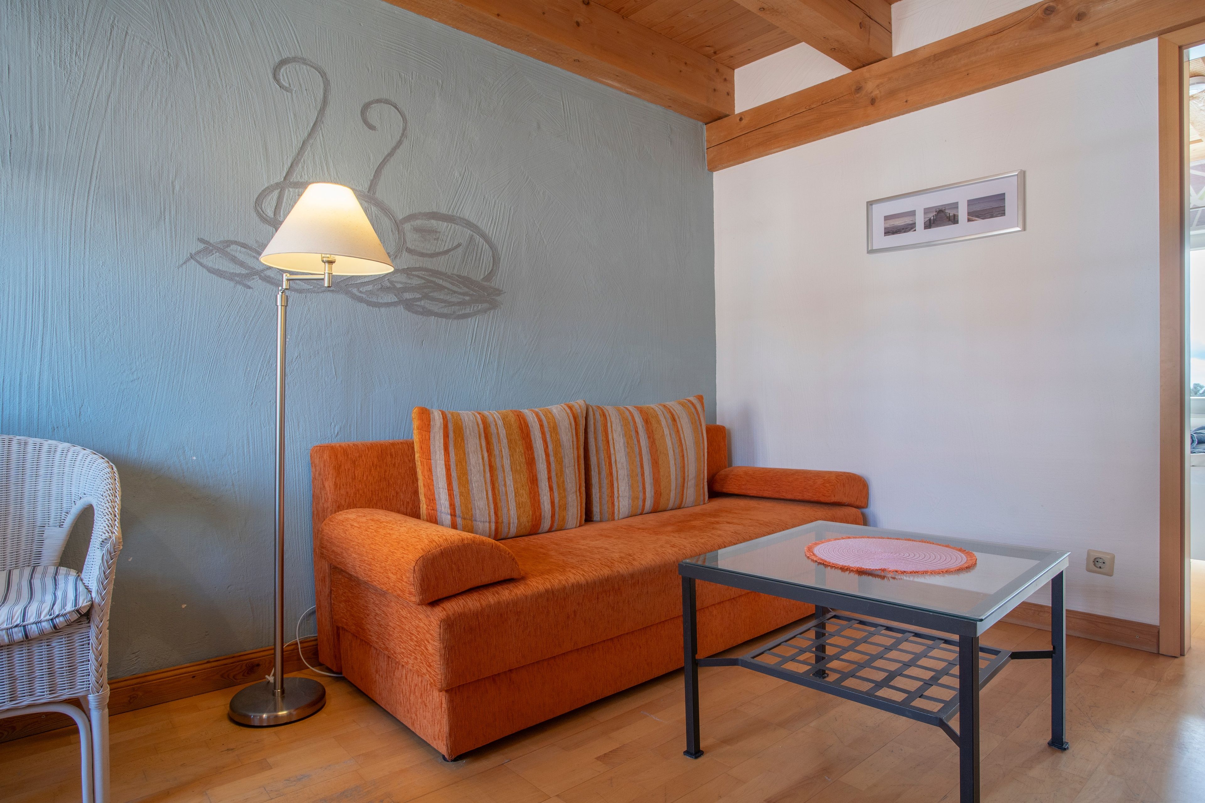 Ein Zimmer mit einer Couch, einer Stehlampe, einem Glastisch und einem Korbstuhl.