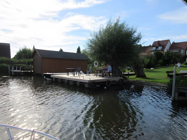 A dock with a table and chairs, a lifebuoy, and a building in the background.