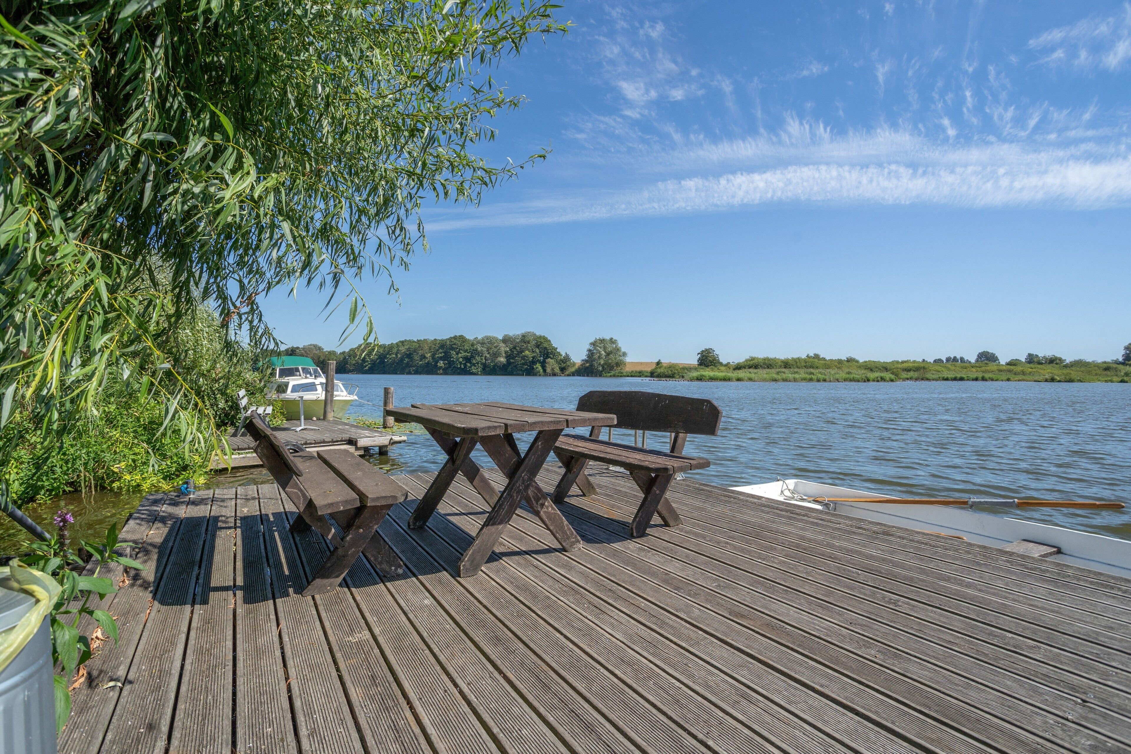 Una terraza de madera con mesas de picnic y un barco fondeado al fondo.