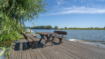 Una terraza de madera con mesas de picnic y un barco fondeado al fondo.