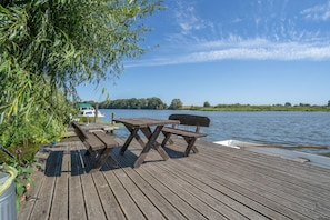 Eine Holzterrasse mit Picknicktischen und einem Boot im Hintergrund.