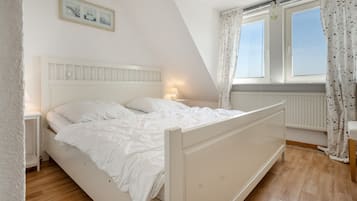 A bedroom with a single bed, a nightstand, a window with curtains, and a wall-mounted picture.