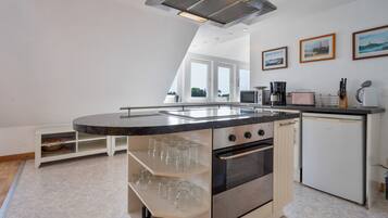 Una cocina moderna con una isla central, horno empotrado y microondas. Hay cuadros enmarcados en la pared y un ventanal que proporciona luz natural.