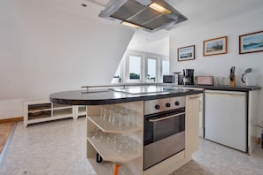 Eine moderne Küche mit einer zentralen Kochinsel, integriertem Backofen und Mikrowelle. An der Wand hängen gerahmte Bilder und ein Fenster sorgt für natürliches Licht.