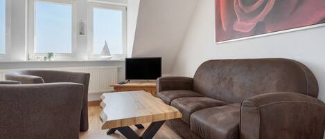 A modern living room with a brown leather sofa, a wooden coffee table, and a large window.