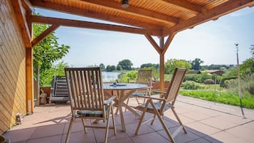 An outdoor patio with a wooden table and chairs, a view of a lake, and a gazebo structure.