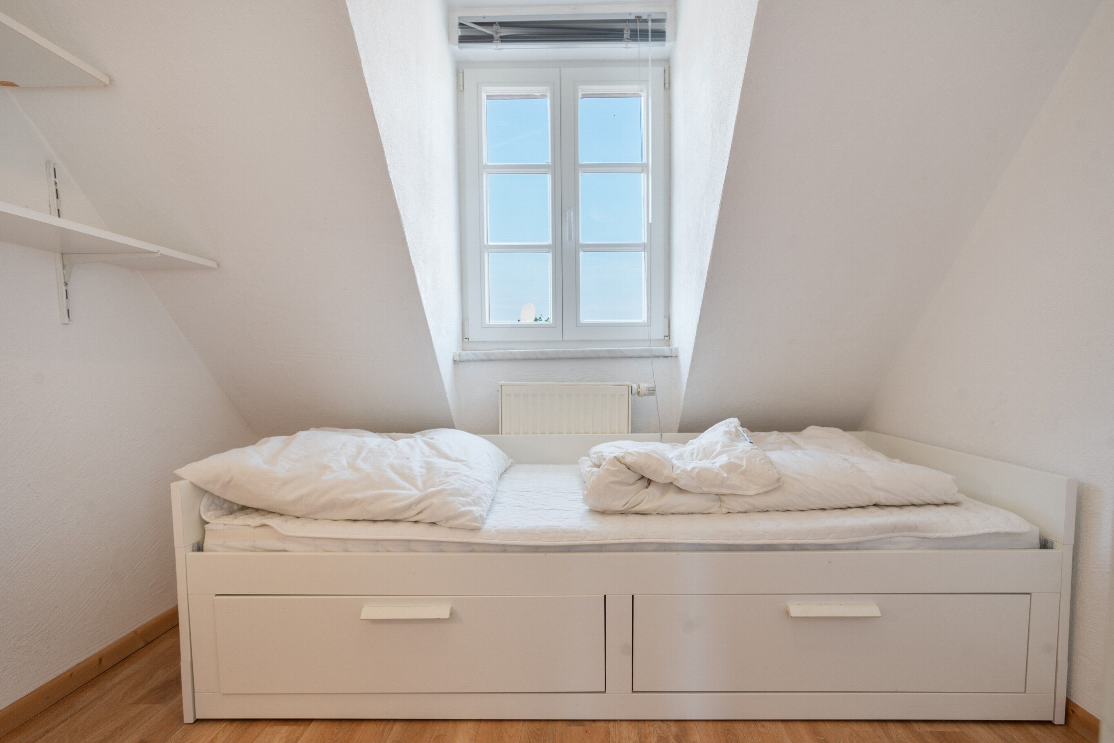 Una habitación pequeña con cama individual, techo inclinado y ventana.