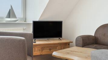 A modern living room with a flat-screen TV on a wooden stand, a sofa, and a dining table.