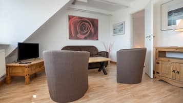 A modern living room with a wooden floor, a brown sofa, a coffee table, a TV, and a painting of a rose.