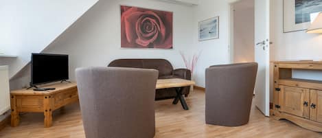 A modern living room with a wooden floor, a brown sofa, a coffee table, a TV, and a painting of a rose.