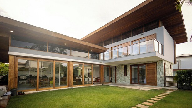 Une maison moderne à deux étages, dotée de grandes portes vitrées, d’une façade en pierre et d’une pelouse bien entretenue.